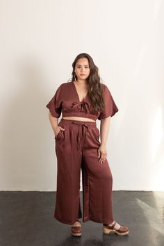 a woman standing in front of a white wall with her hands on her hips and wearing brown