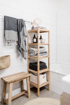 a bathroom with white tile and wooden shelves filled with towels, toiletries and bathtub