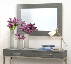 two vases with purple flowers are on a table next to a mirror and lamp