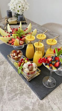 a table topped with fruit and drinks on top of a black tray next to glasses