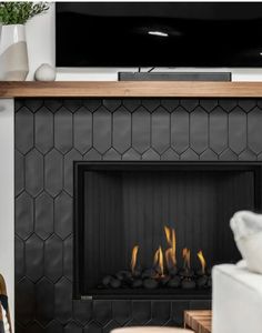 a living room with a fire place and television on the wall above it is decorated in black tiles