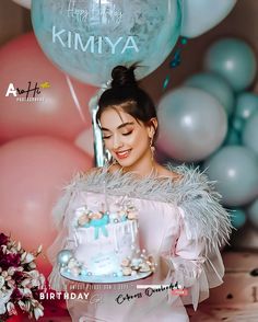 a woman holding a birthday cake in front of balloons and streamers with the words happy birthday kimiya on it