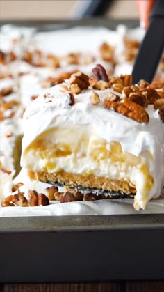 a piece of cake with white frosting and pecans on top is being lifted from the pan