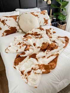 a cow print blanket laying on top of a bed next to pillows and a pillow