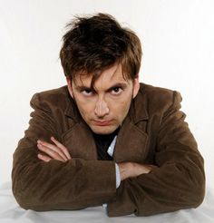 a man with his arms crossed posing for the camera while wearing a brown jacket and tie