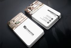 two white business cards sitting on top of a black table with an image of a building in the background