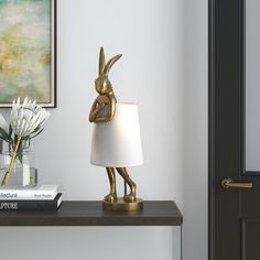 a gold rabbit lamp sitting on top of a table next to a vase with flowers