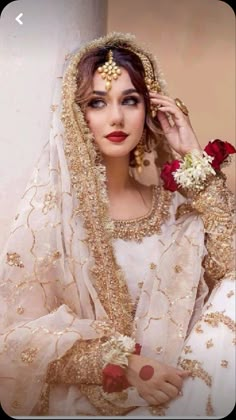 a woman wearing a white and gold bridal outfit with red flowers in her hair