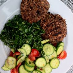 a white plate topped with meat patties and veggies next to a salad