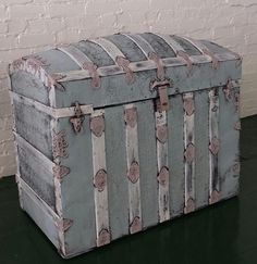 an old trunk sitting on the floor in front of a white brick wall and green floor