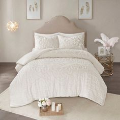 a bed with white comforter and two candles on the end table next to it