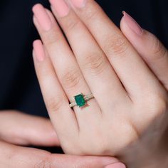 a woman's hand holding a ring with a green stone on it and two other hands