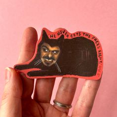 a hand holding up a small sticker with a cat on it's face