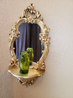 two green vases sitting on top of a shelf in front of a gold mirror