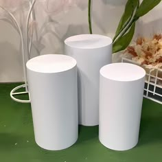 three white vases sitting on top of a green table