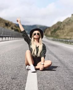 a woman sitting on the side of a road with her hand up in the air