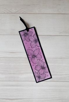 a purple bookmark with flowers on it sitting on a white table next to a black cord