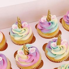 cupcakes with pastel frosting and unicorn horn decorations on them in a box