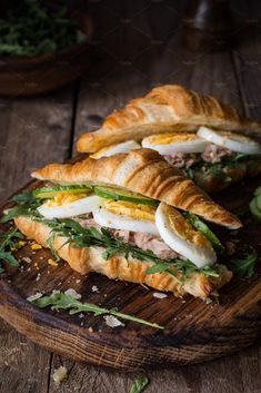 a sandwich with meat, cheese and greens on a cutting board