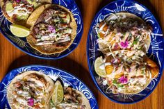 three plates filled with tacos and other food on top of a wooden table,