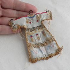 a hand is holding an embroidered doll with fringes