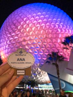 a person holding up a small sign in front of the spaceship dome at disney world