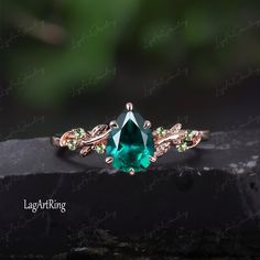 an emerald colored ring with green and white stones on it's sides, sitting on top of a rock