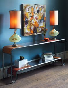 a console table with two lamps and a painting on the wall