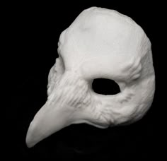 a white mask that looks like a bird's head is on a black surface