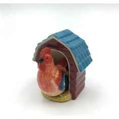 a ceramic chicken in a small red and blue hut on a white background with the door open