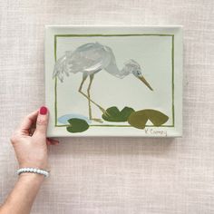 a person holding up a painting on a canvas with water lillies and a bird