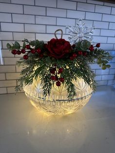 a glass bowl filled with flowers and greenery on a counter top next to a brick wall