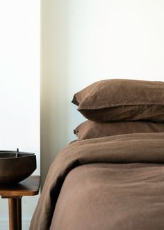 a bed with two pillows and a bowl on the end table in front of it