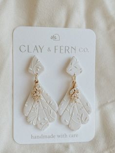 a pair of white and gold earrings on top of a white cloth covered bed sheet