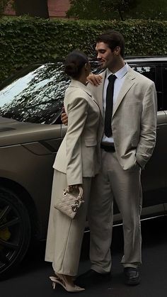 a man and woman standing in front of a car with their arms around each other