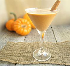 a glass filled with liquid sitting on top of a wooden table next to an orange pumpkin