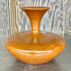 a wooden vase sitting on top of a metal table next to a wooden wall and floor