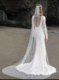 a woman in a white wedding dress with a veil on her head is walking down the beach