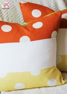 two orange and white polka dot pillows sitting on top of a bed next to each other