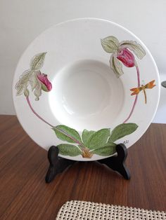 a white bowl with flowers painted on the side sitting on a table next to a place mat