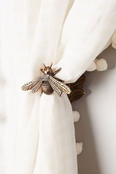 a close up of a white curtain with a gold bee on it's side