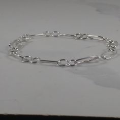 Every link in this silver chain is soldered for strength, with a hand-made silver hook and eye fastening to keep it securely on your wrist. The design features figure-of-eight shapes linked by ovals of round section sterling silver wire. You can adjust the length to suit your wrist by linking the hook into different eyes. Sterling Silver Link Paperclip Bracelet With Lobster Clasp, Sterling Silver Link Paperclip Bracelet, Minimalist Sterling Silver Bracelets With Hook And Links, Minimalist Sterling Silver Bracelet With Hooks And Links, Sterling Silver Oval Link Chain Bracelet, Sterling Silver Bracelet With Cable Chain, Modern Sterling Silver Bracelet With Cable Chain, Sterling Silver Paperclip Link Bracelet, Sterling Silver Bracelet With Paperclip Chain