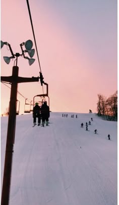 a ski lift with people skiing down the hill at sunset or dawn in the background