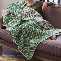 a woman sitting on a couch under a green and white knitted blanket with holes in it