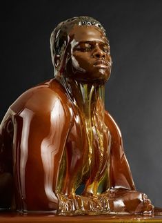 a brown statue sitting on top of a wooden table next to a black wall and floor