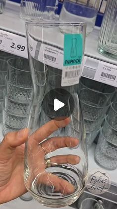 a person is holding a glass in front of some glasses on the shelf at a store