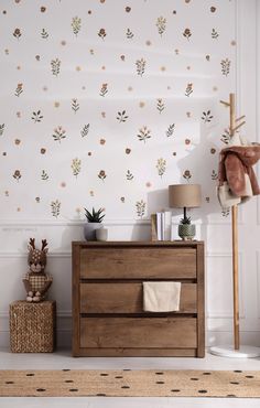 a wooden dresser sitting in front of a wall with flowers on it and a lamp next to it