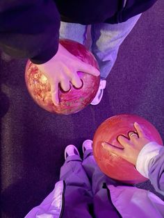 two people are holding bowling balls with their hands on top of one another and the other hand reaching for them