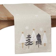 a white christmas table runner with trees and snowflakes on the top, hanging from a wooden shelf