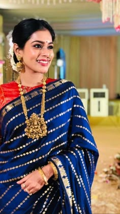 a woman in a blue and red sari with gold jewelry on her neck, smiling at the camera